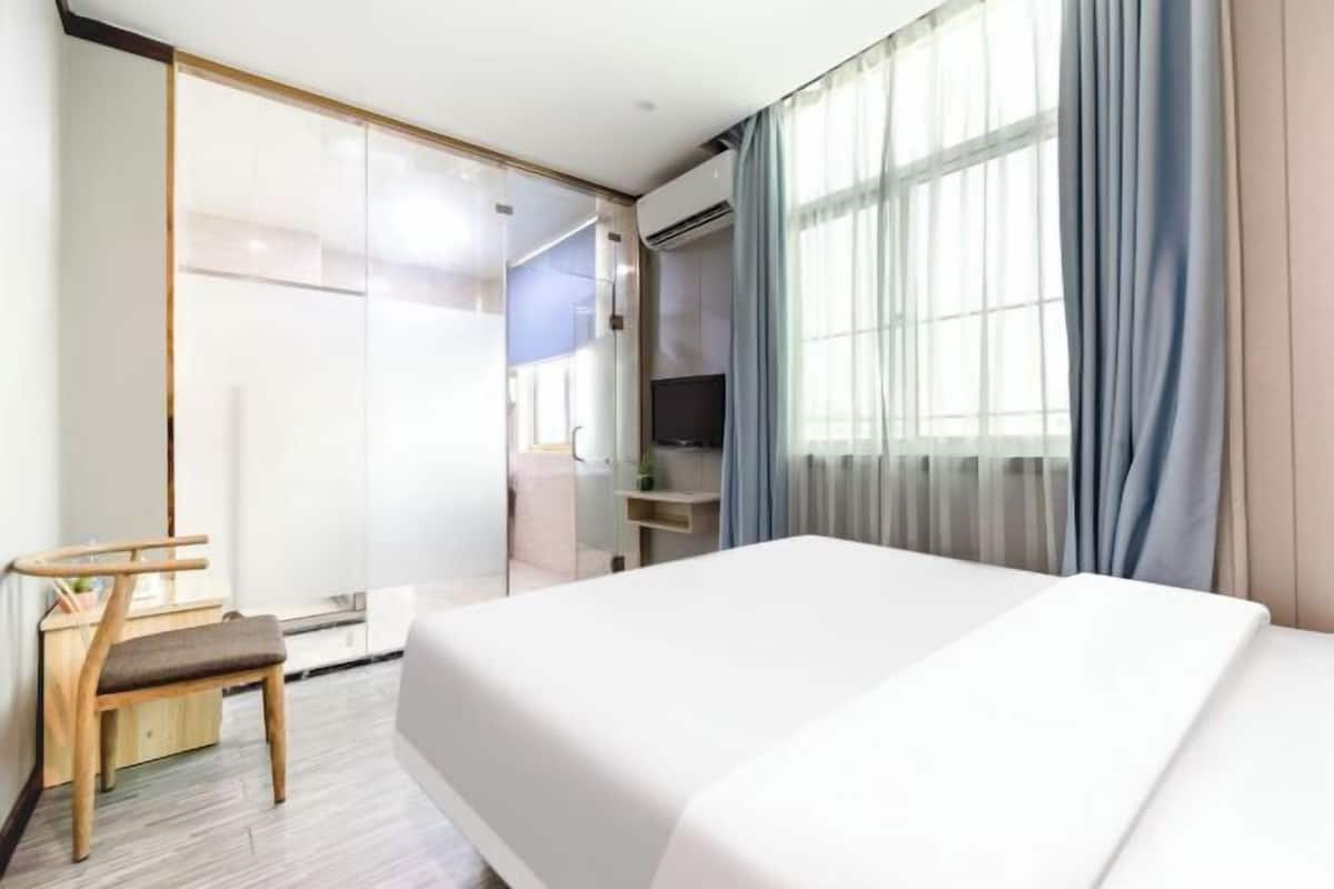 A hotel room with a bed, a desk, a chair, and a large window with curtains.
