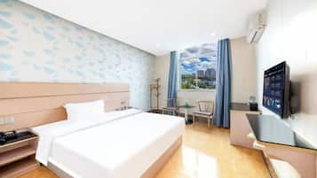 A hotel room with a bed, a desk, a TV, and a window with a city view.