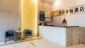 A hotel reception area with a marble counter, two blue armchairs, and a decorative wall.
