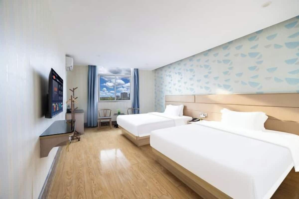 A hotel room with two beds, a desk, a TV, and a window with a view.