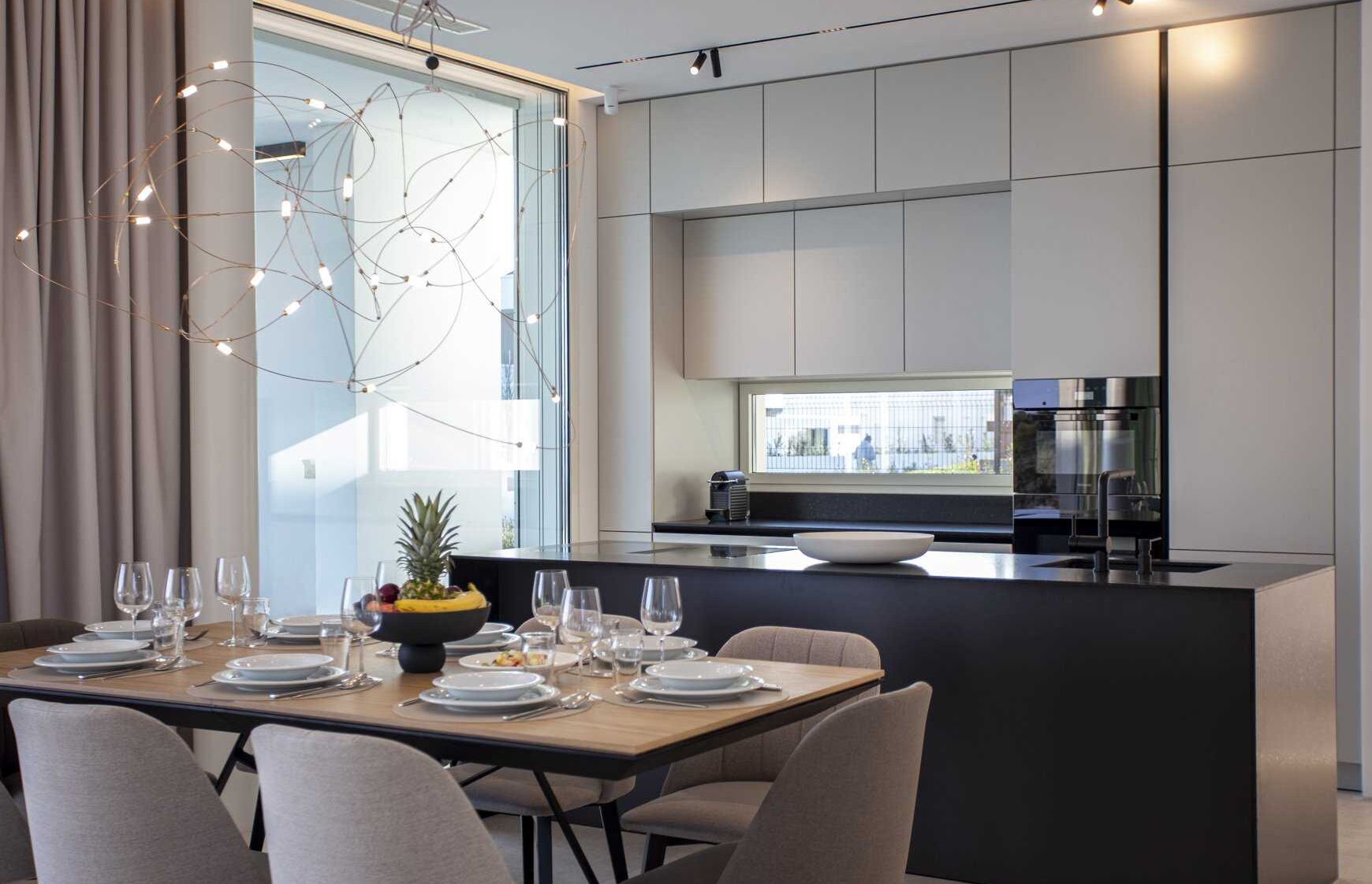 A modern kitchen with a central island, a dining area with a table set for four, and a large window providing natural light.