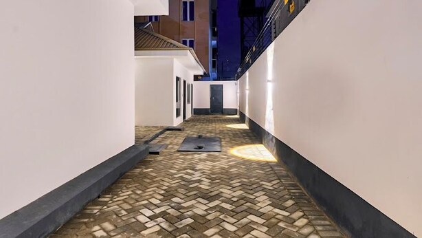 A narrow alleyway with a patterned tile floor, white walls, and a building in the background. - Stone House Apartment  (Abuja)