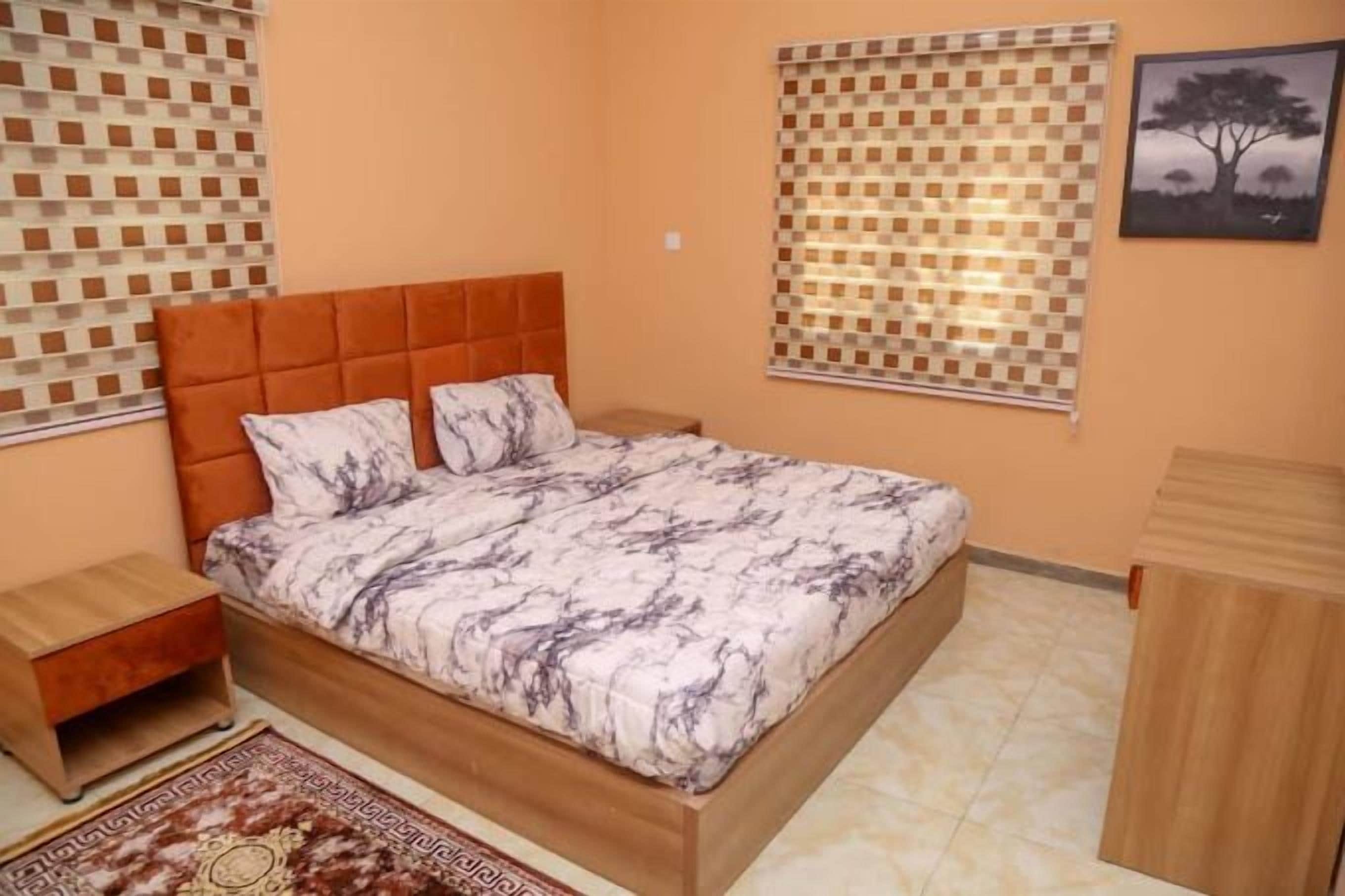A bedroom with a bed, a nightstand, a wooden cabinet, patterned curtains, and a framed picture on the wall.