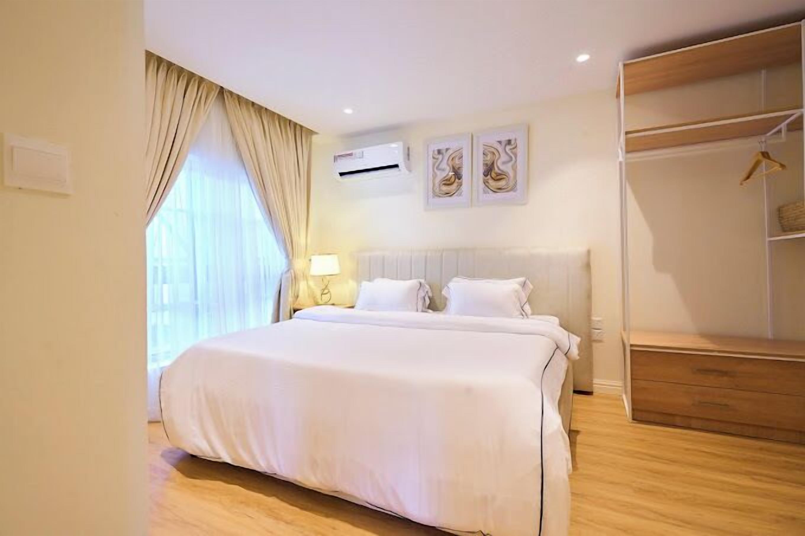 A hotel room with a large bed, a wardrobe, a bedside table with a lamp, and two wall-mounted air conditioning units.