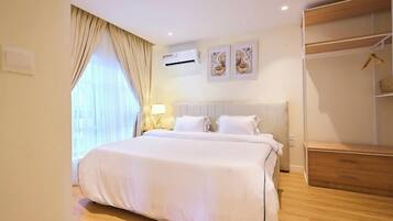 A hotel room with a large bed, a wardrobe, a bedside table with a lamp, and two wall-mounted air conditioning units.