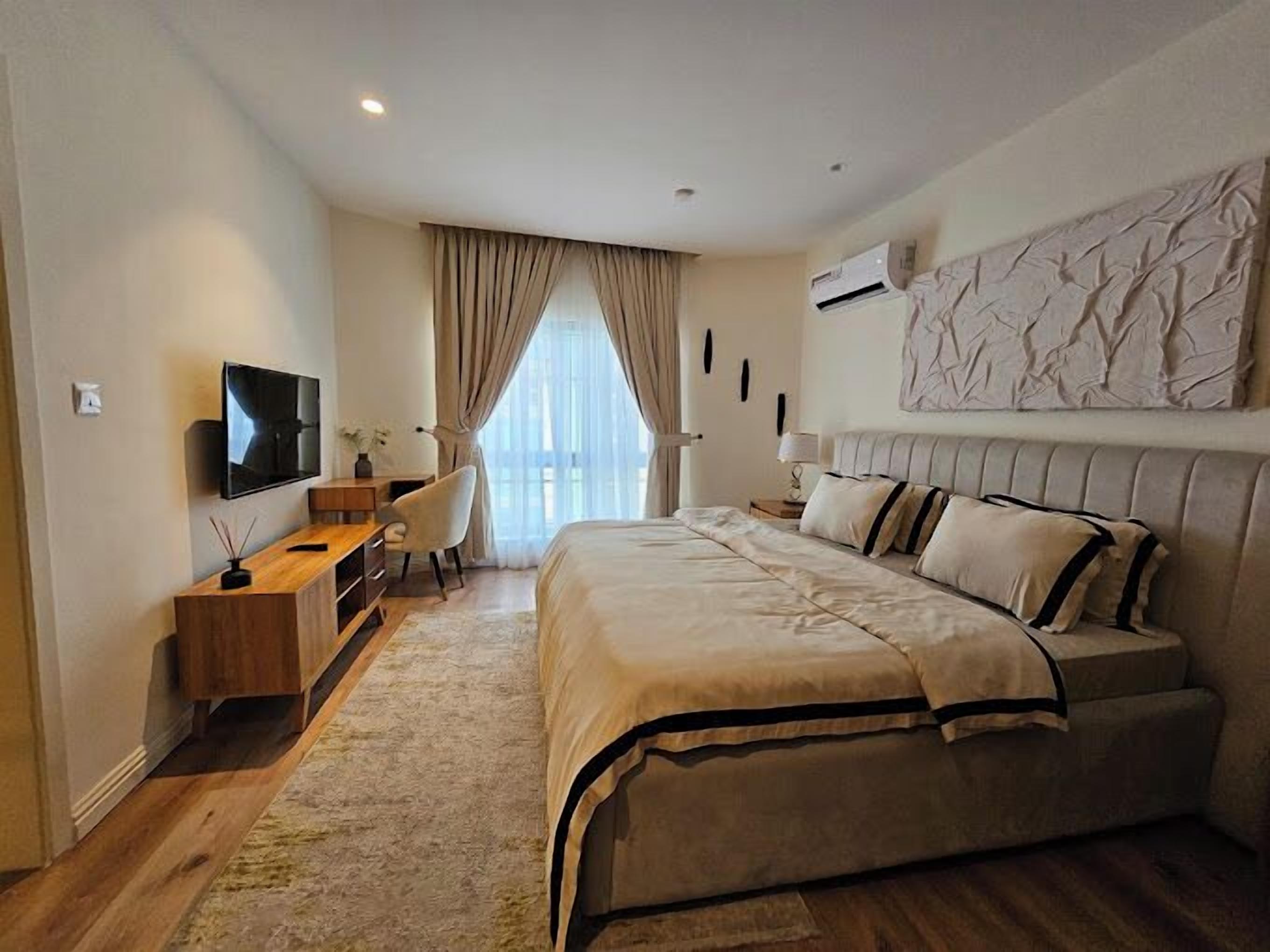 A modern bedroom with a large bed, a desk, a chair, and a TV.