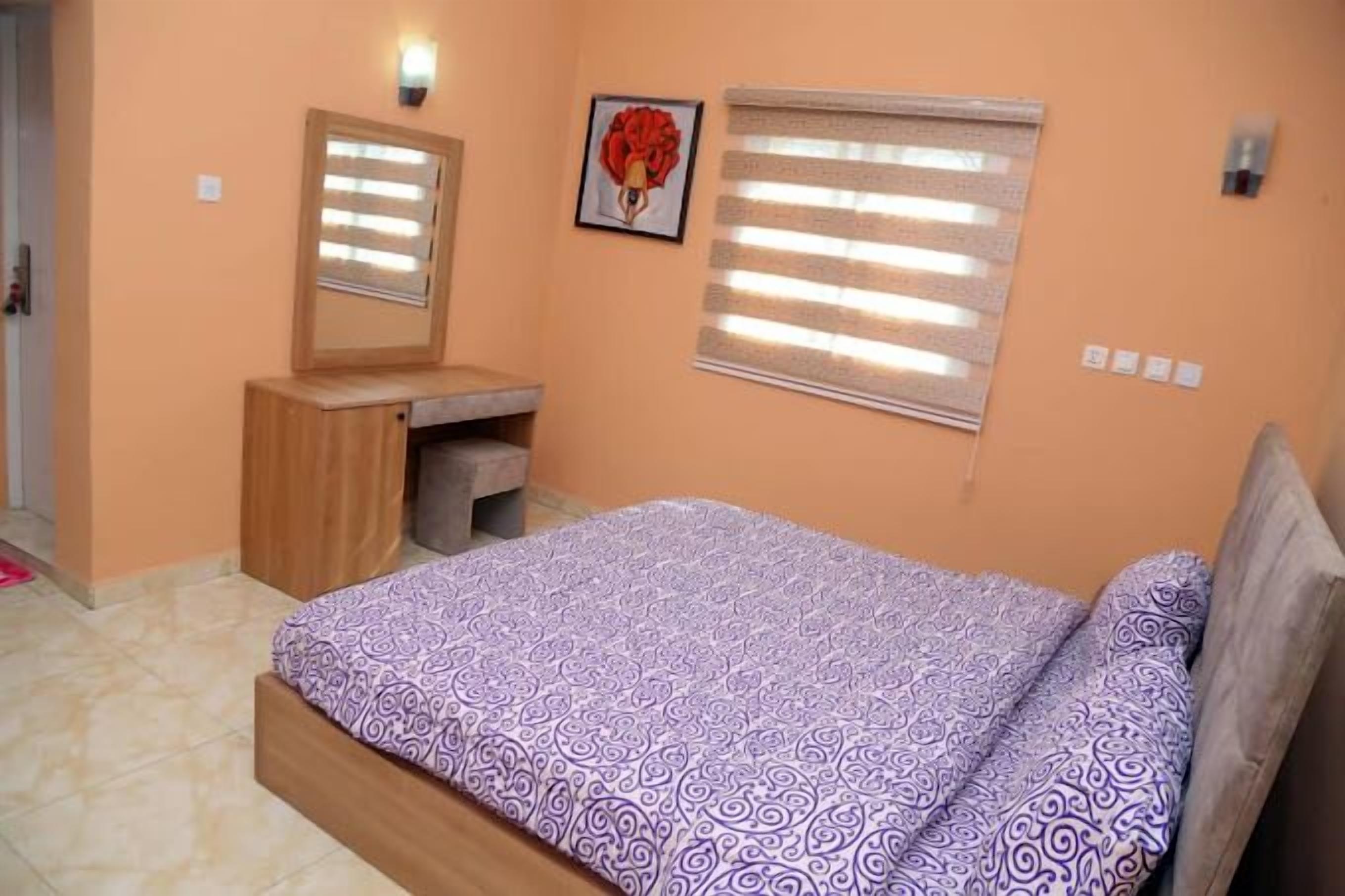 Ein Schlafzimmer mit einem Bett, einem Holztisch, einem Spiegel und einem Fenster mit Jalousien.