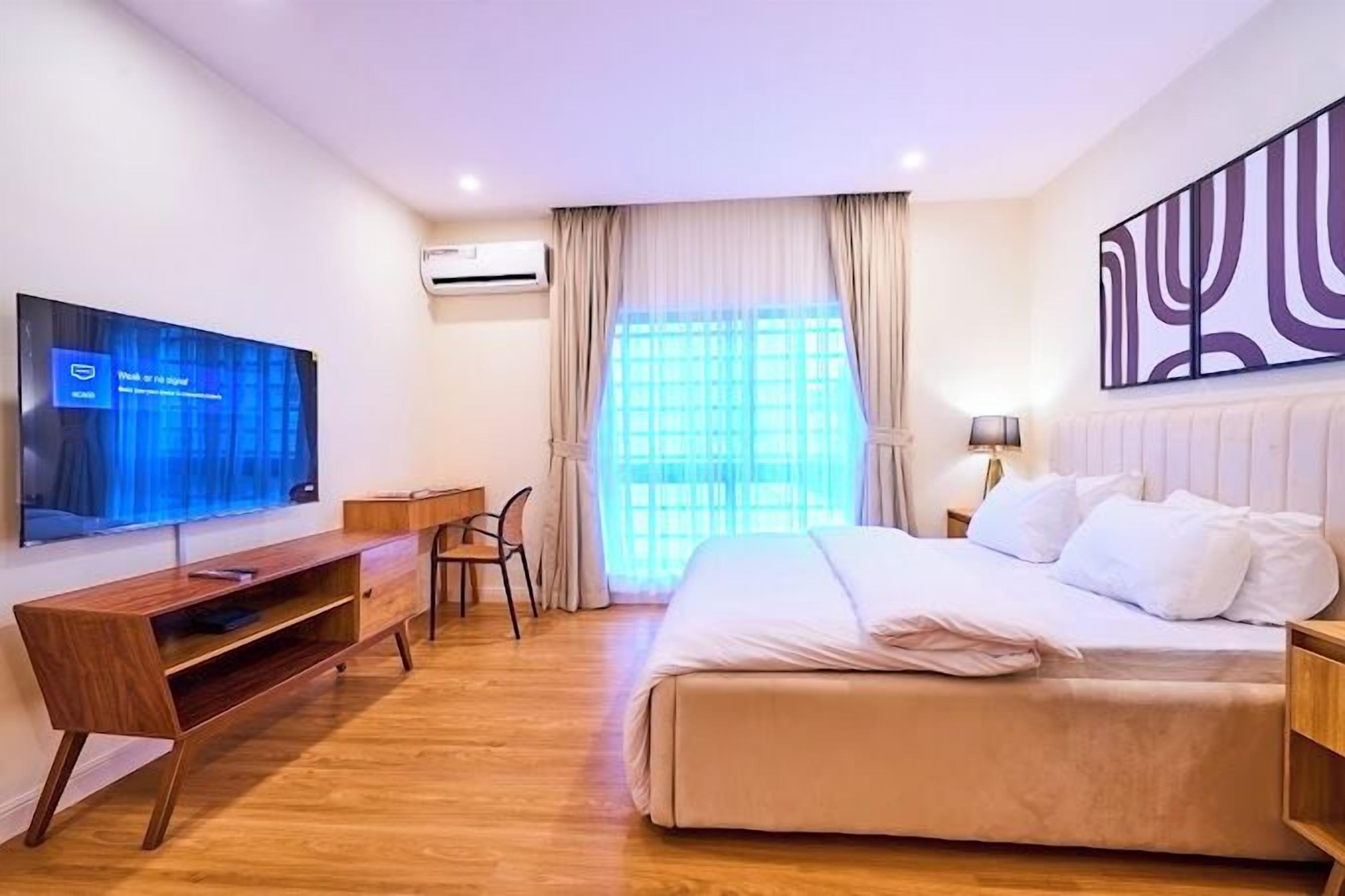 A modern hotel room with a large bed, a TV on the wall, a desk, and a window with curtains.