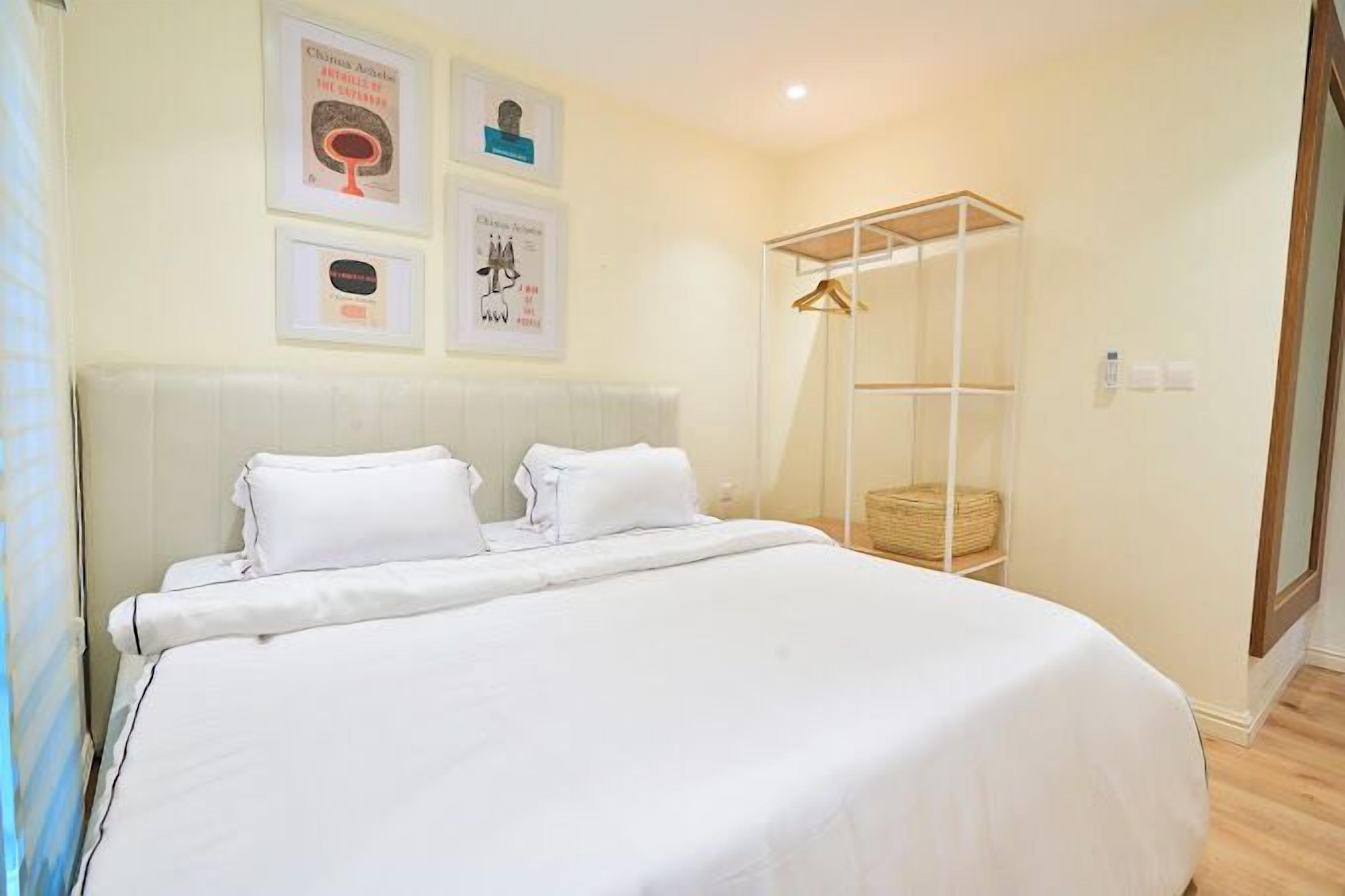 A neatly made bed with white linens, a bedside table with a lamp, and a wall-mounted shelf with a basket.