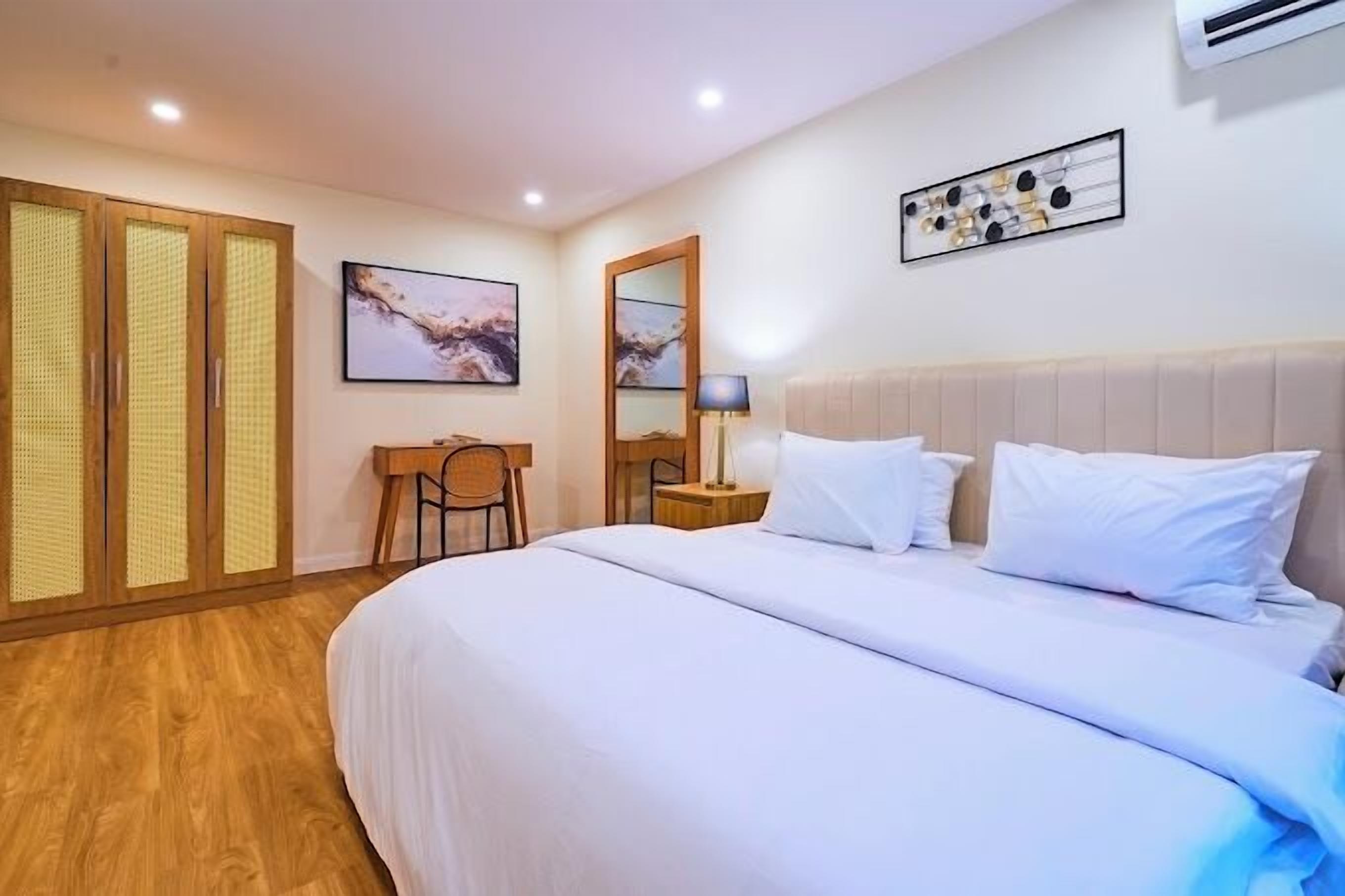A hotel room with a bed, a desk, a chair, a lamp, and a large mirror.