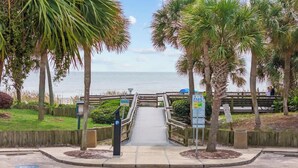 A pathway leading to a beach with palm trees and a wooden fence. - Flip-Flop Hideaway 1BR (Myrtle Beach)