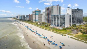 A beachfront hotel with multiple high-rise buildings, a sandy beach, and umbrellas. - Flip-Flop Hideaway 1BR (Myrtle Beach)