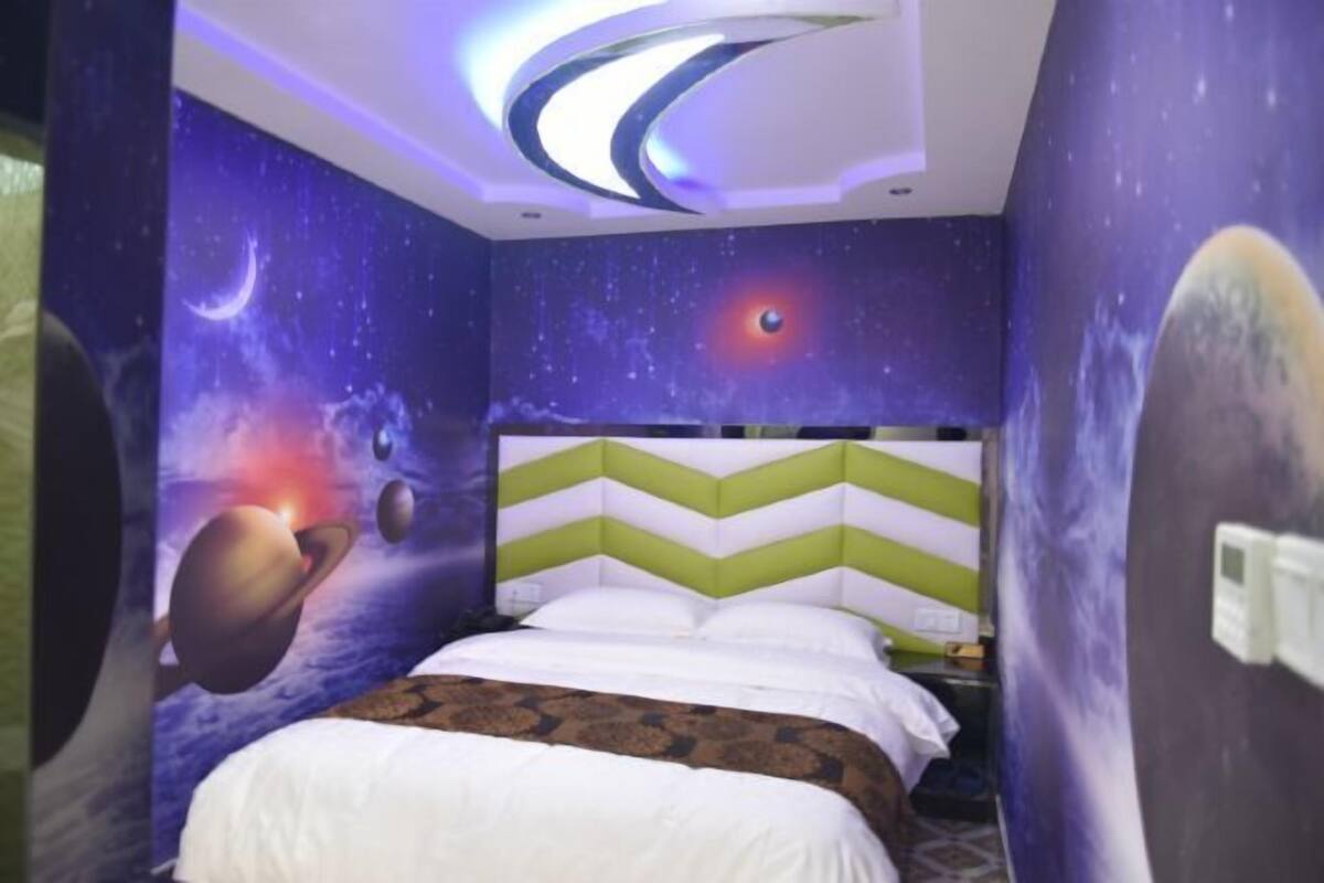 A bedroom with a space-themed mural, a green and white chevron-patterned headboard, and a bed with white bedding.