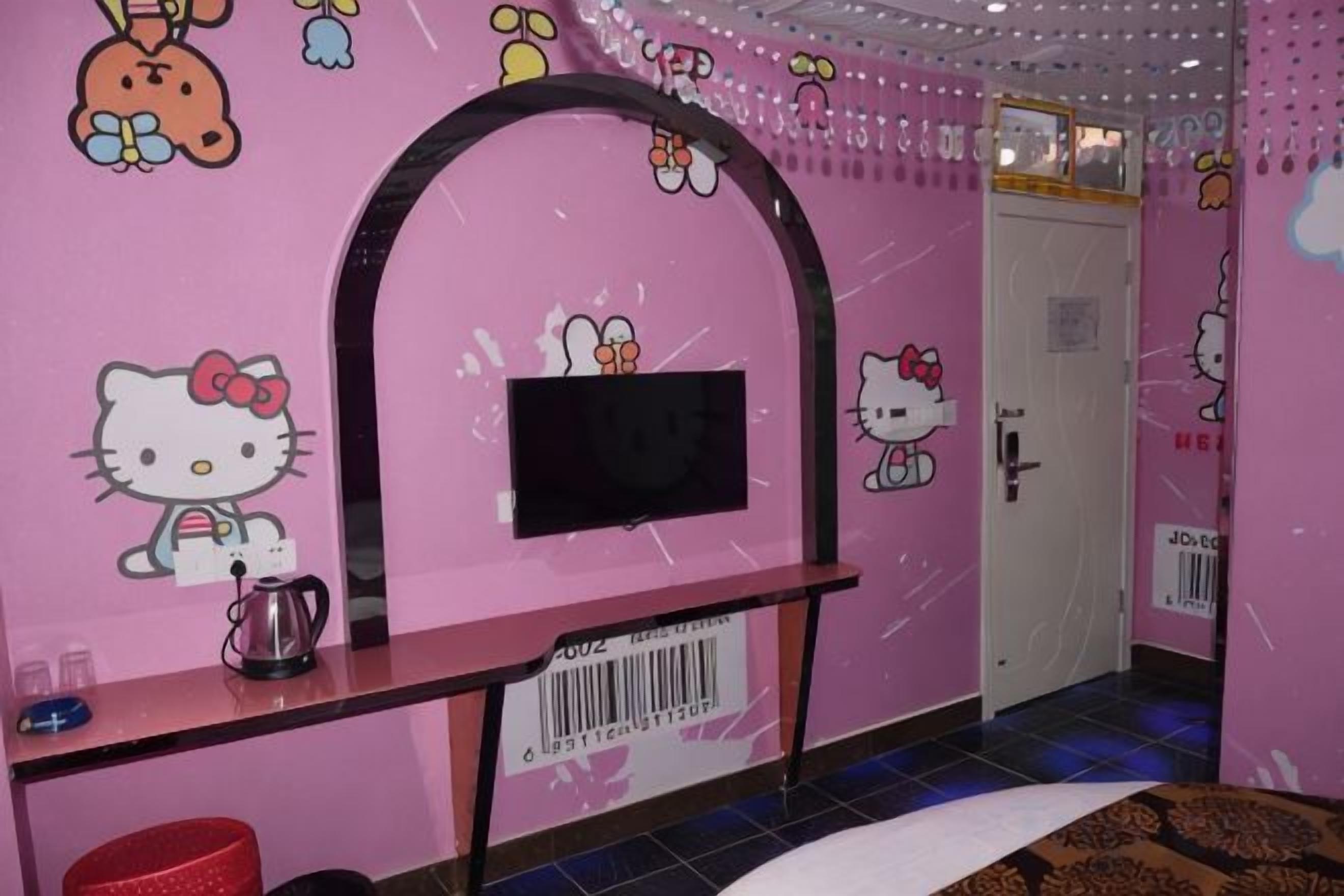 Een roze kamer met een aan de muur bevestigde televisie, een tafeltje met een waterkoker en een deur met slot.