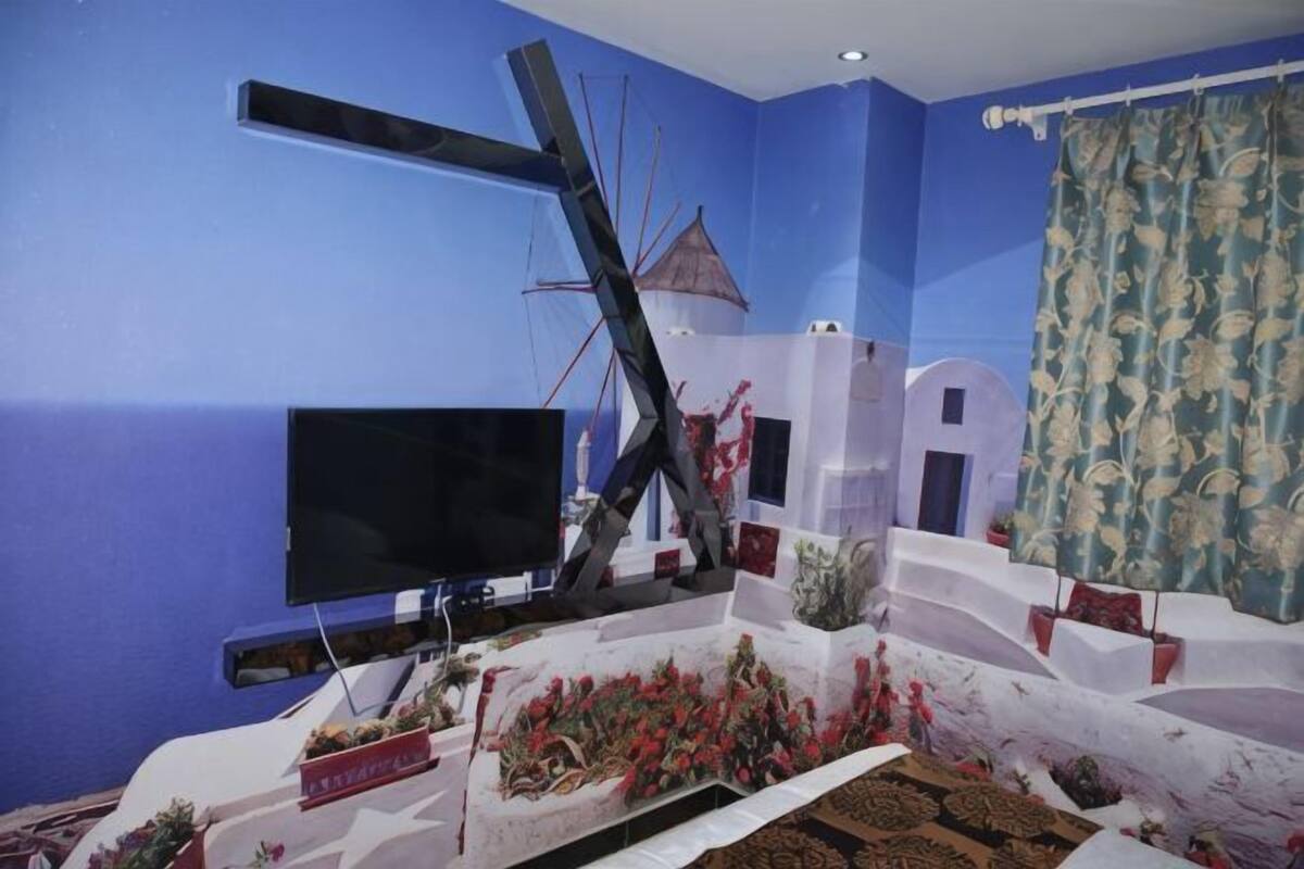 A room with a TV, a large abstract sculpture, and a patterned curtain.