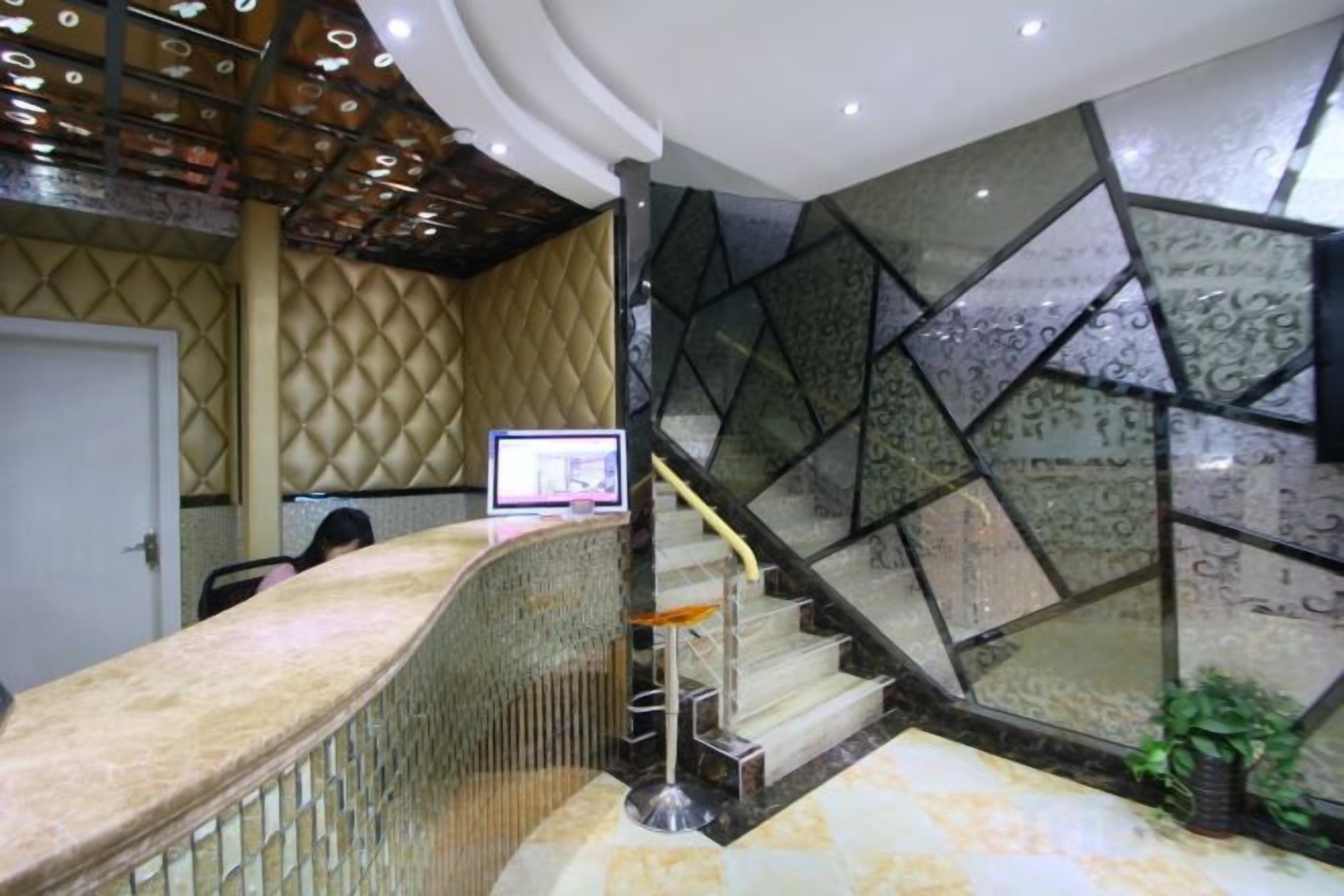 Uma área de recepção com balcão curvo, escada com painéis de vidro e uma porta ao fundo.