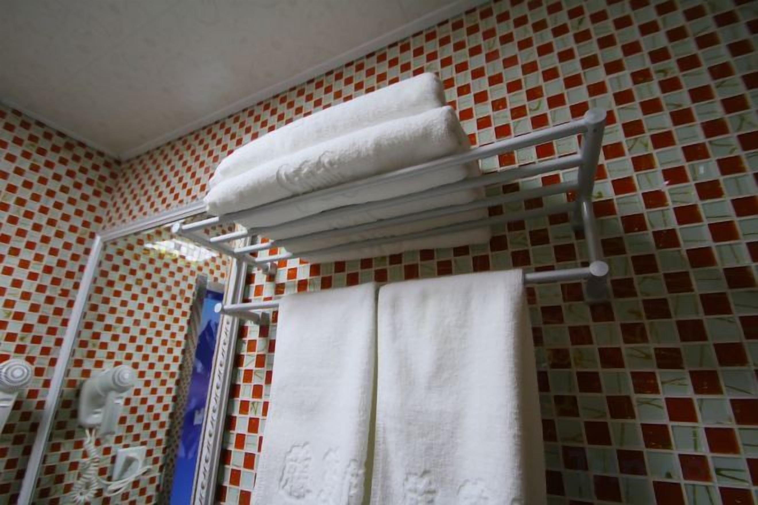 A bathroom with a tiled wall, a towel rack with folded towels, and a mirror.