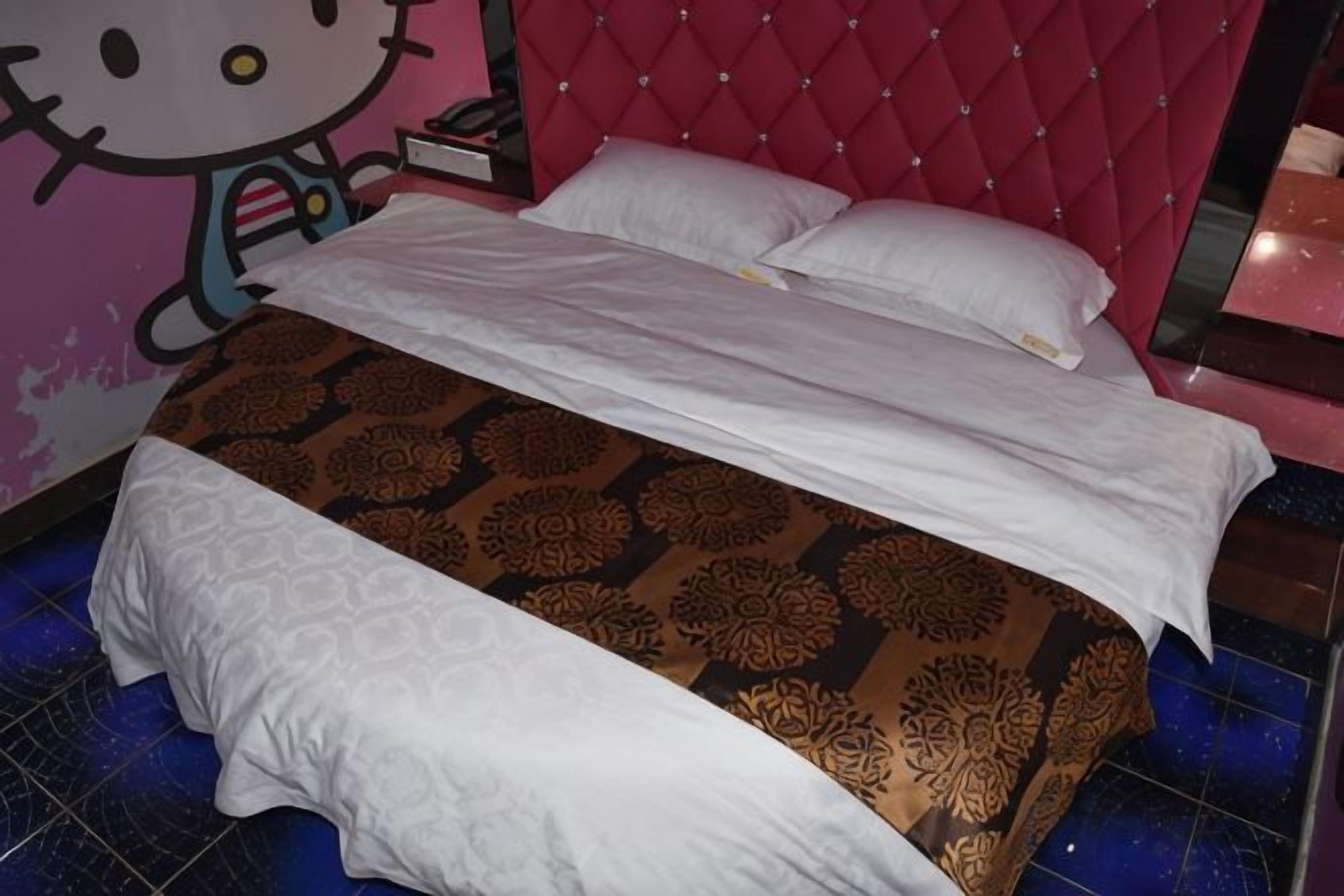 Uma cama com colcha estampada, cabeceira estofada vermelha e decoração de parede com tema Hello Kitty.