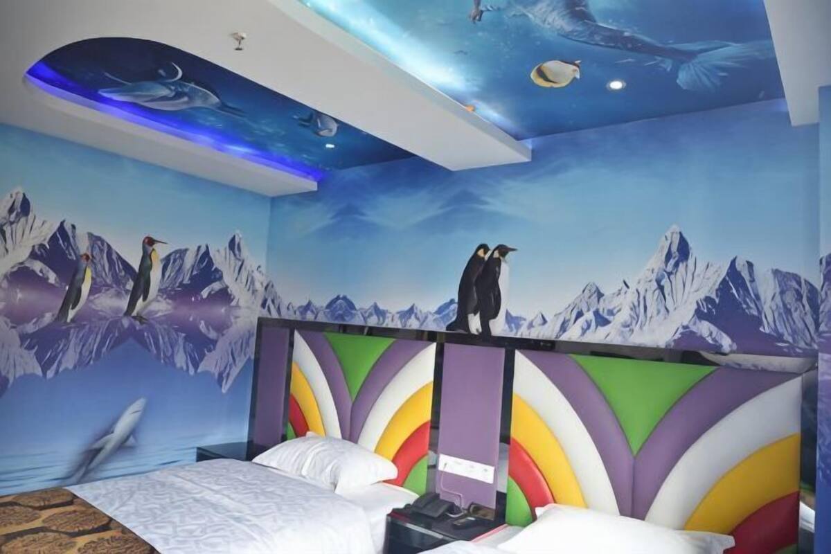 A room with a bed, a colorful headboard, a mural of mountains, and a ceiling with a fish design.