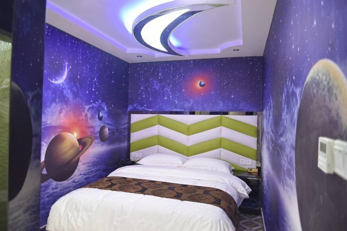A bedroom with a bed, a green and white chevron-patterned headboard, and a wall mural of space with planets and stars.