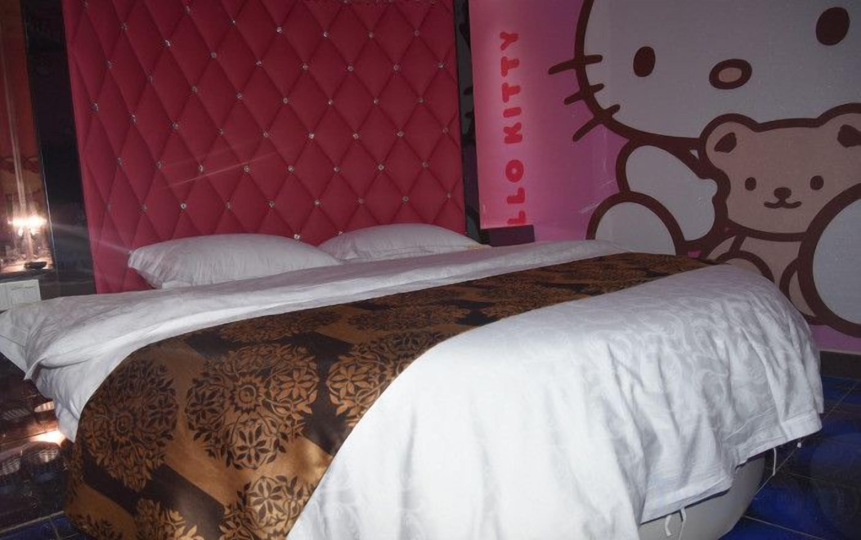 A bed with a patterned bedspread, a pink headboard, and a Hello Kitty wall decoration.