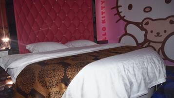 A bed with a patterned bedspread, a pink headboard, and a Hello Kitty wall decoration.