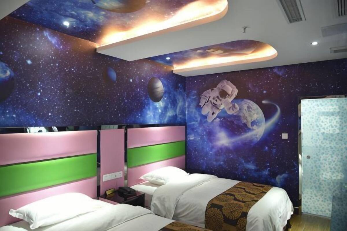 A bedroom with a space-themed mural, a bed with a green headboard, and a nightstand.