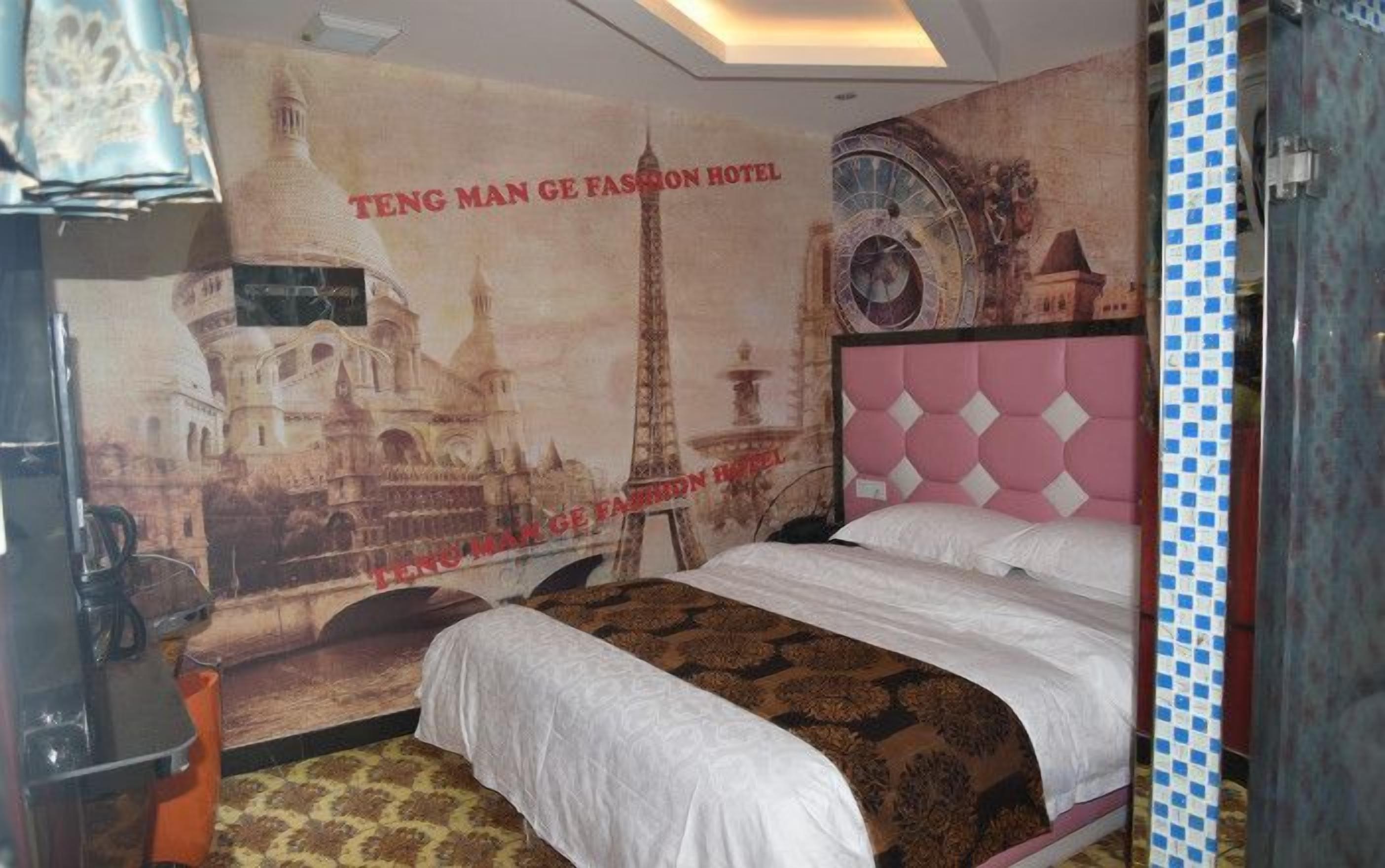 A hotel room with a bed, a poster of a cityscape, and a patterned carpet.
