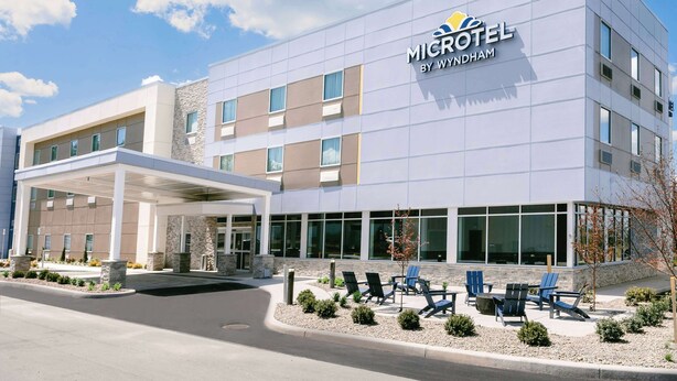 A modern Microtel hotel by Wyndham with a covered entrance, outdoor seating area, and a clear sky. - Microtel Inn & Suites by Wyndham Newark NY (Newark)