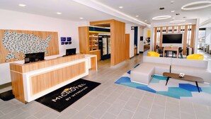 A modern hotel lobby with a reception desk, seating area, and a large TV screen. - Microtel Inn & Suites by Wyndham Newark NY (Newark)