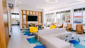 A modern lobby with a large seating area, a TV mounted on the wall, and a view of the outside through large windows. - Microtel Inn & Suites by Wyndham Newark NY (Newark)