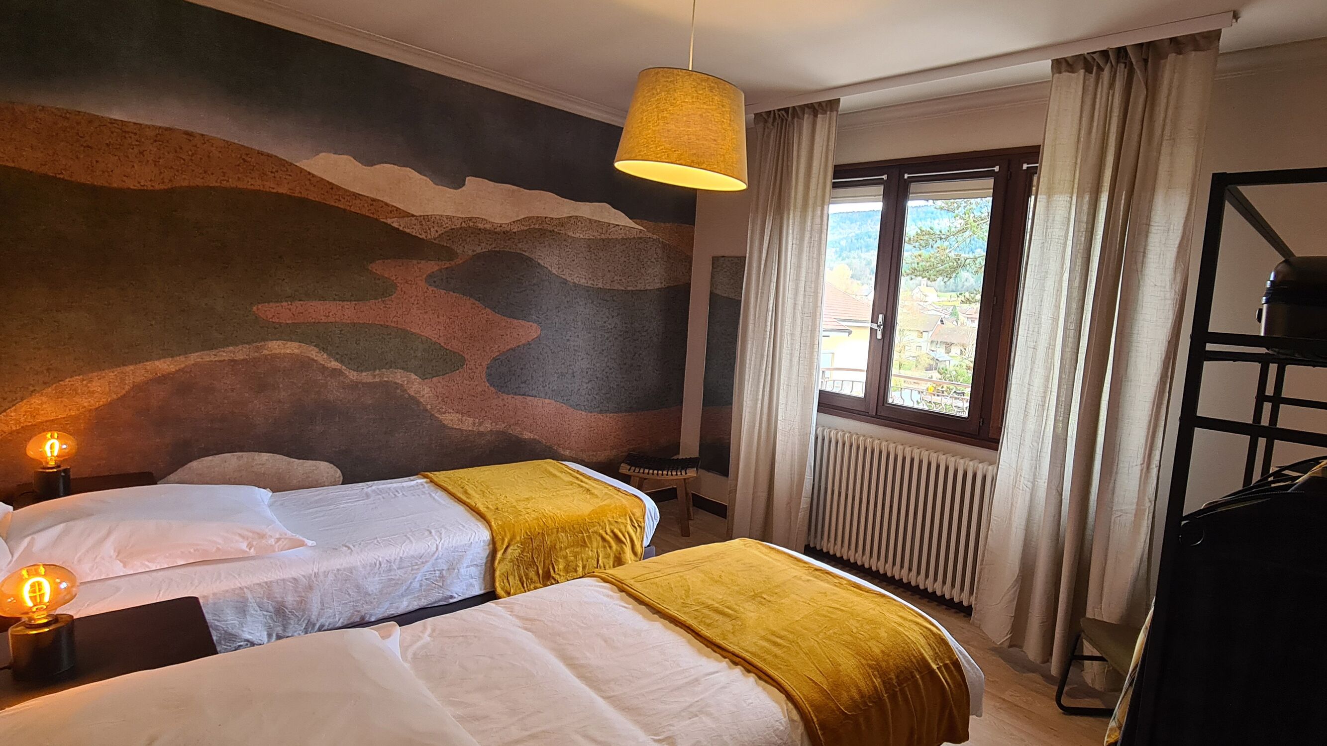 Habitación de hotel con dos camas, un mural grande en la pared, una ventana con cortinas y un radiador.