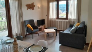A modern living room with a sofa, a chair, a TV, and a dining area with a table set for two. - Apartment in quiet house between lakes and fir trees (MARTIGNAT)