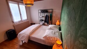 A bedroom with a bed, a radiator, a suitcase, a clothing rack, and a window. - Apartment in quiet house between lakes and fir trees (MARTIGNAT)