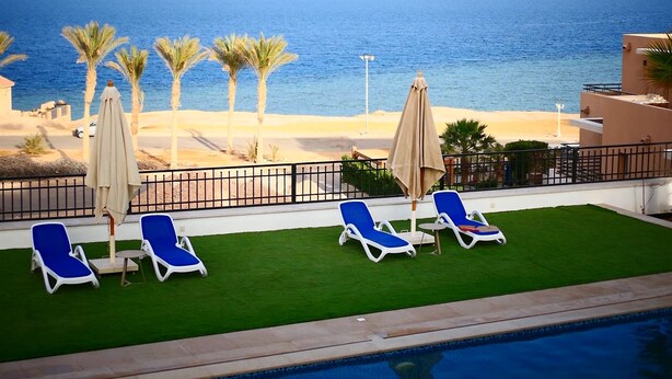 A poolside view with lounge chairs and umbrellas, a clear view of the ocean, and a well-maintained lawn.