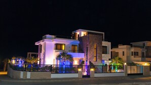 A modern two-story house with a balcony, illuminated by colorful lights.