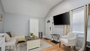 Ein kompakter Wohnraum mit Sofa, einem kleinen Esstisch, einem an der Wand montierten Fernseher und einem weißen Sessel.