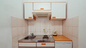 A compact kitchen with a sink, stove, and dishwasher, featuring white cabinets and a tiled backsplash.