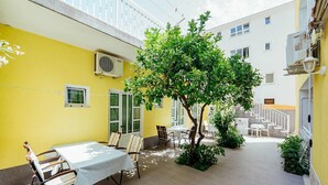 A courtyard with a dining table and chairs, surrounded by yellow walls and a tree.