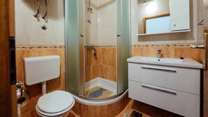 A bathroom with a glass-enclosed shower, a toilet, a sink, and a mirror above the sink. - Apartments Pezo - Studio  ( Tina 3) (Baška Voda)