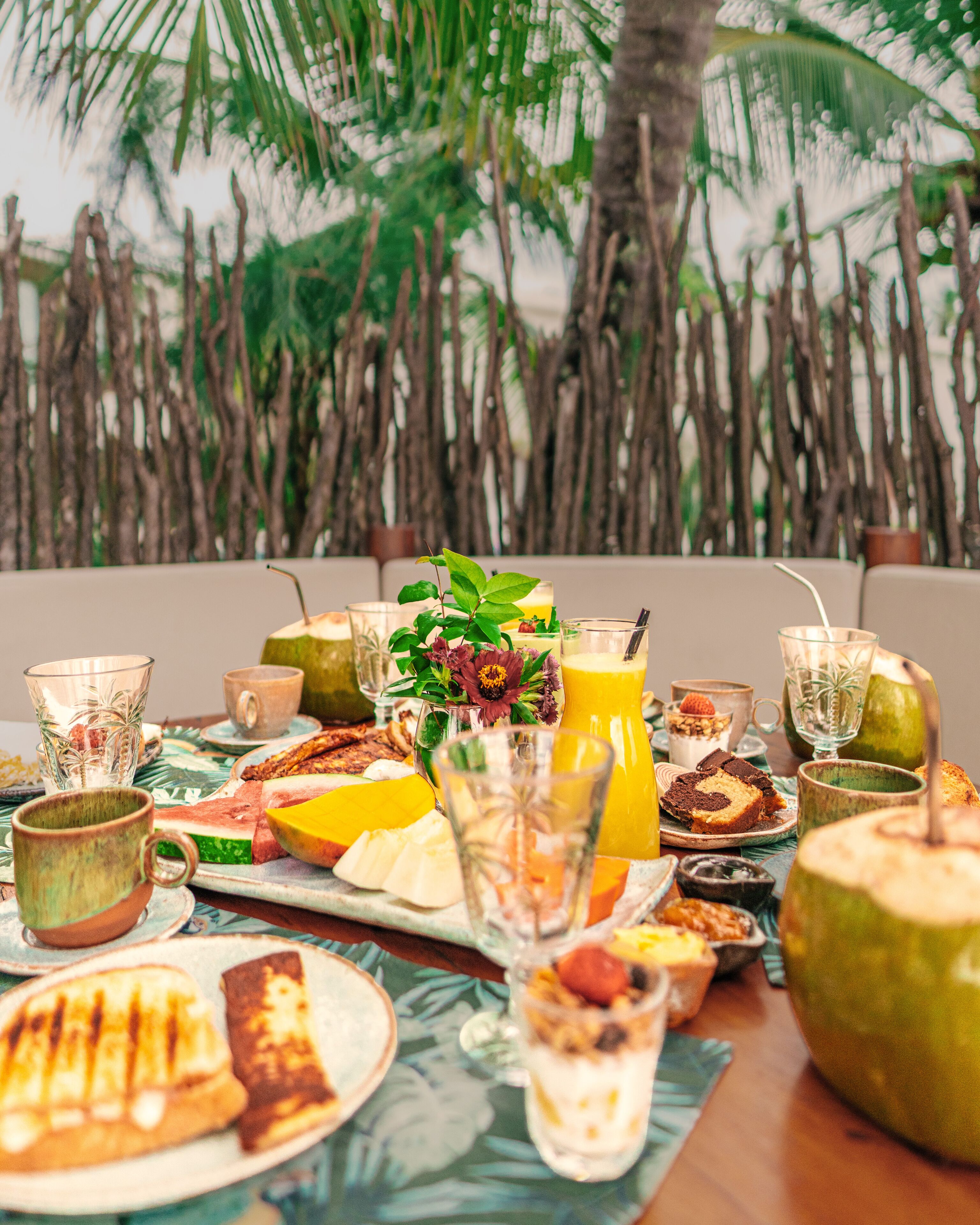 Un bufé de desayuno con diversos alimentos y bebidas, con palmeras de fondo.