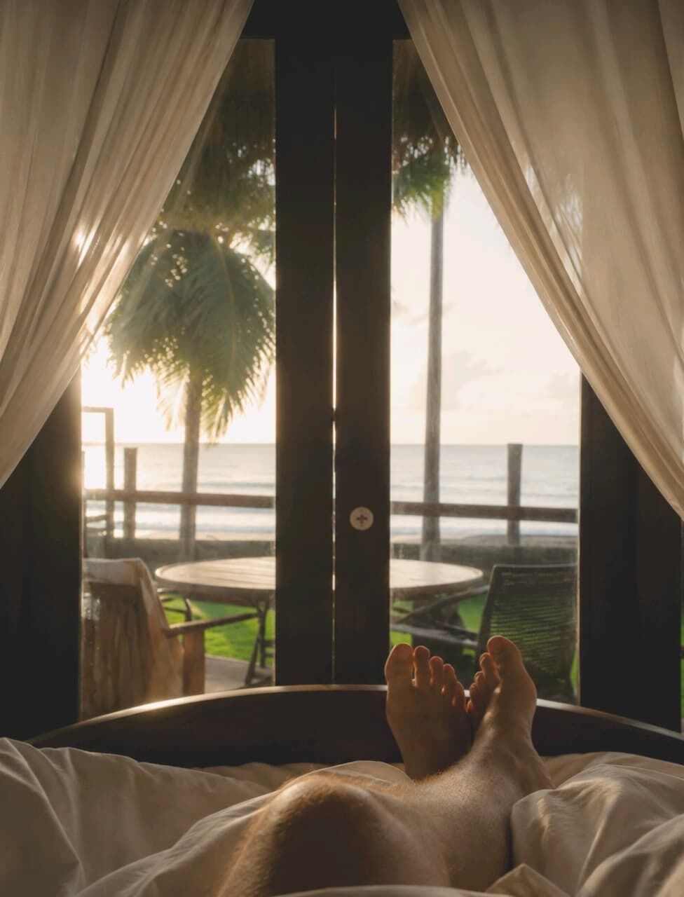 Quarto com uma cama, vista para o mar e uma palmeira lá fora.