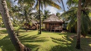 Un resort tropical con cabañas de techo de paja, palmeras y un césped bien cuidado.
