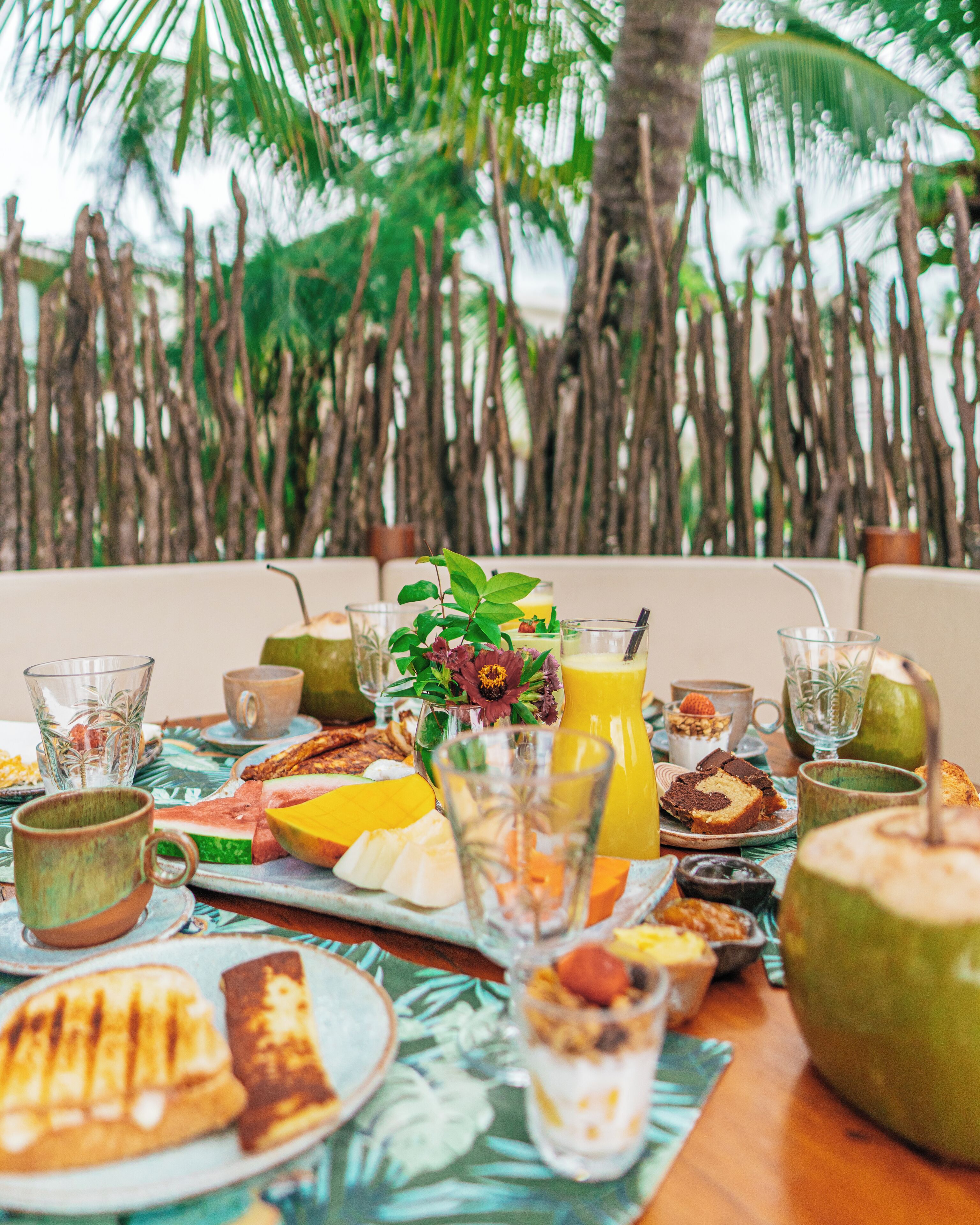 Un bufé de desayuno con diferentes alimentos y bebidas, con palmeras de fondo.