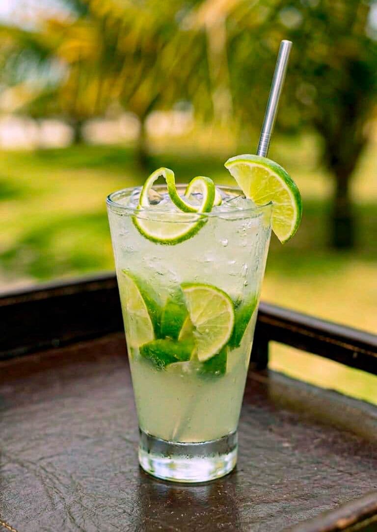 A glass of a clear beverage with lime slices and mint leaves, with a straw, on a wooden surface.