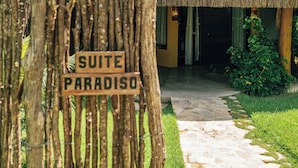 A thatched-roof structure labeled 'SUITE PARADISO' with a stone pathway leading to it, surrounded by greenery.