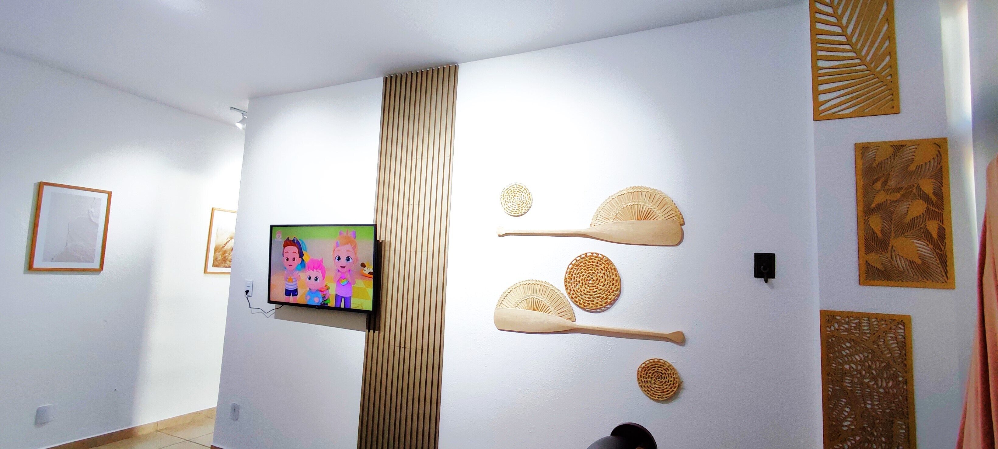 Una habitación con televisión montada en la pared, detalles decorativos en la pared y un separador de listones de madera.