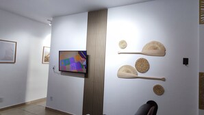 A room with a television mounted on the wall, decorative wall art, and a vertical wooden panel. - Beachfront Apartment, Sea View, Garage, 2 Bedrooms, WI-FI, Cable TV, NETFLIX etc. (Arraial do Cabo)