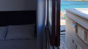A room with a bed, a window, and a view of a beach and buildings. - Beachfront Apartment, Sea View, Garage, 2 Bedrooms, WI-FI, Cable TV, NETFLIX etc. (Arraial do Cabo)