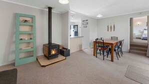 Una sala de estar moderna con una chimenea de leña, un comedor con mesa y sillas de madera, y una escalera que conduce a otro nivel.